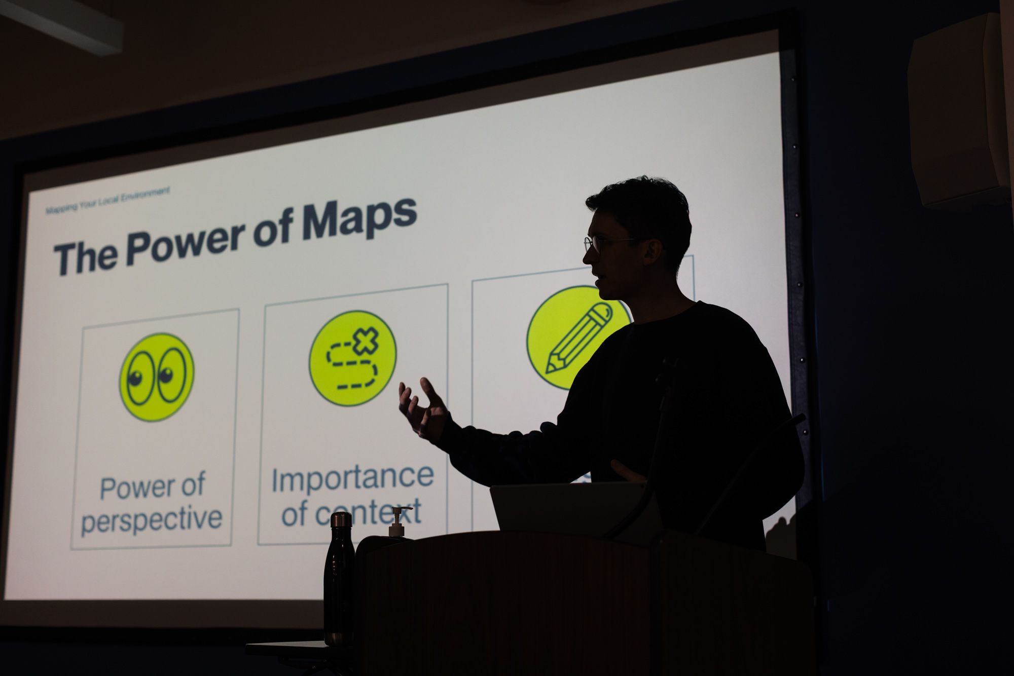 Facilitator stands in front of a presentation about the Power of Maps