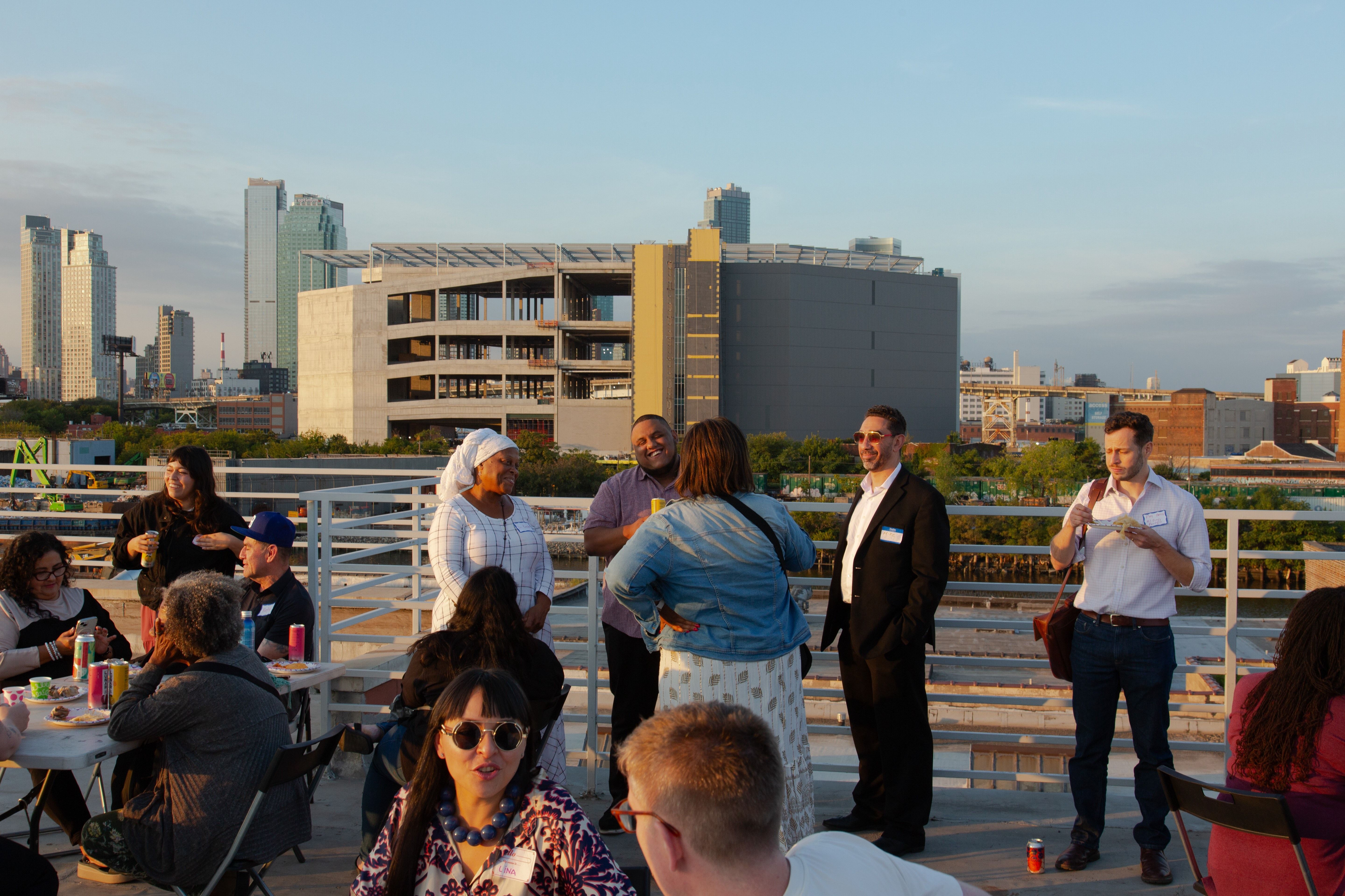 Several groups of people in conversation with city skyline in the background.