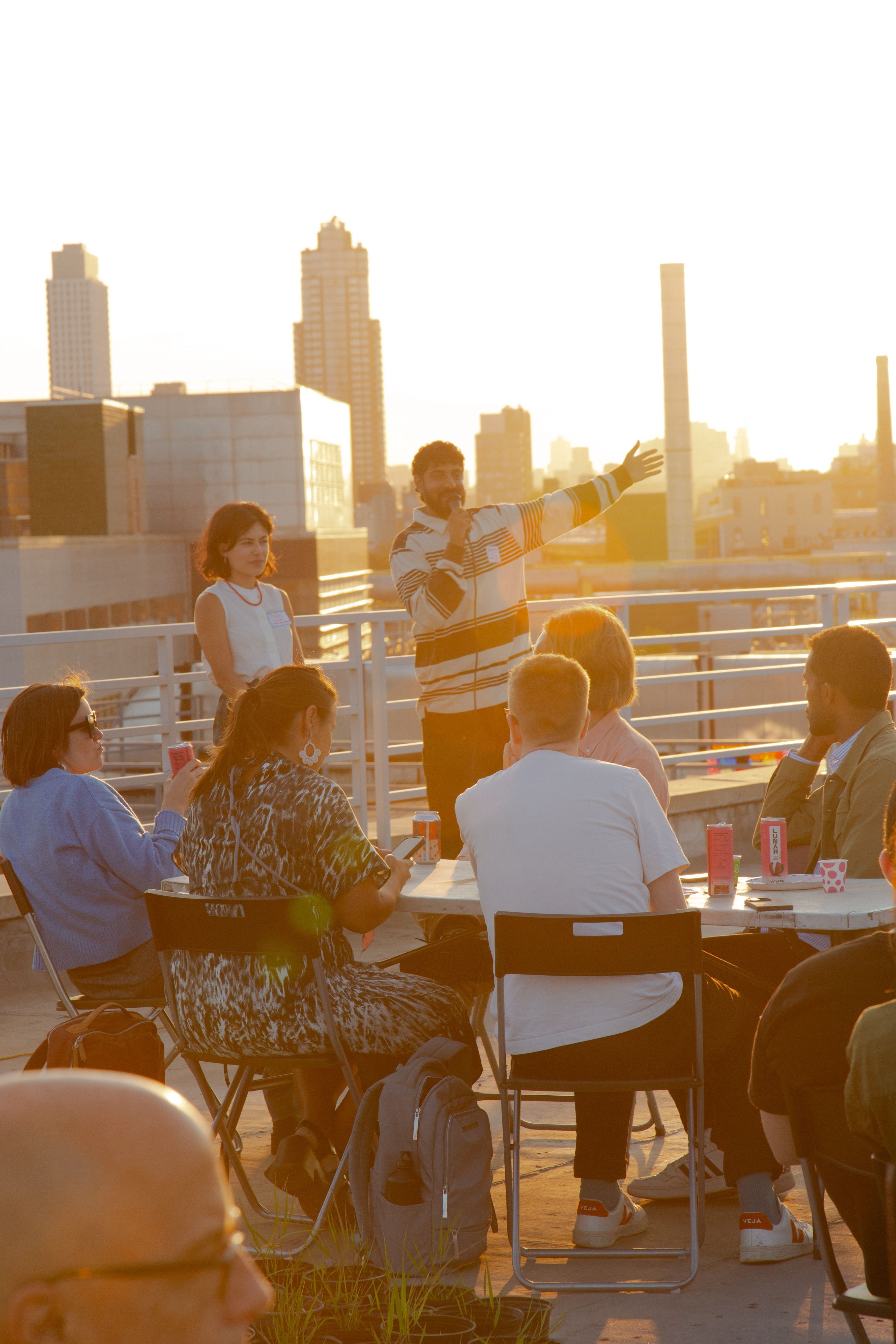 Arpan Somani speaking on a microphone with arm outstretched, alongside Tara Pham, as they address an audience with sunset-lit city skyline behind them.